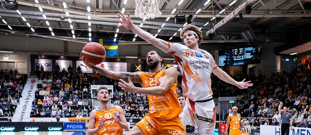 Basketspelare i orange och vitt hoppar mot korgen inför en fullsatt läktare.
