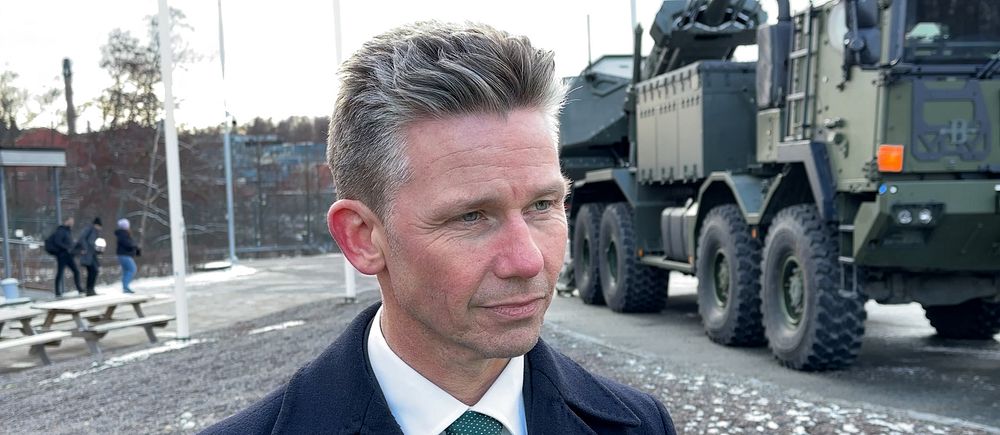 Man i kostym står framför ett militärfordon på en snöig väg.
