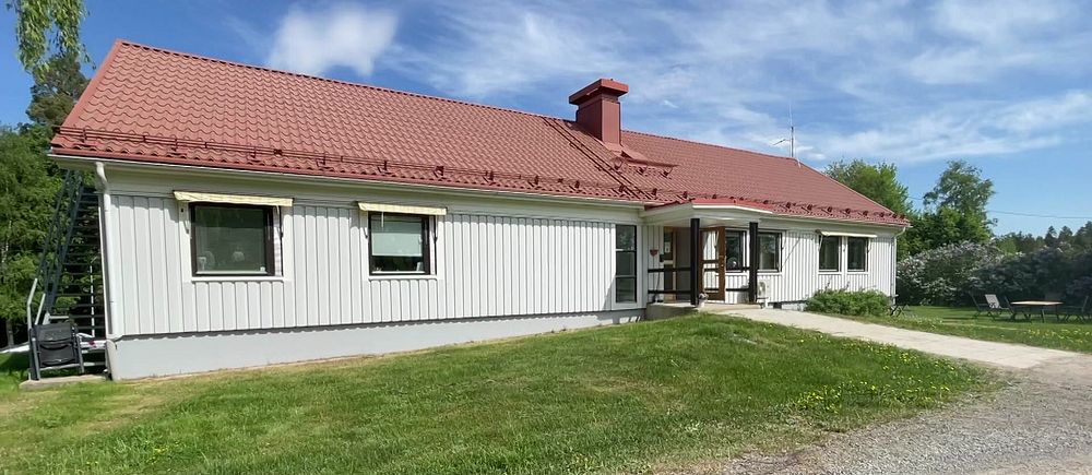 Ett vitt hus med tegeltak på en solig dag. Gräs och grusgata i förgrunden.