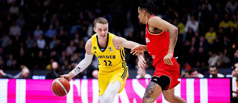 Basketspelare från Sverige dribblar mot en spelare i rött under en match.