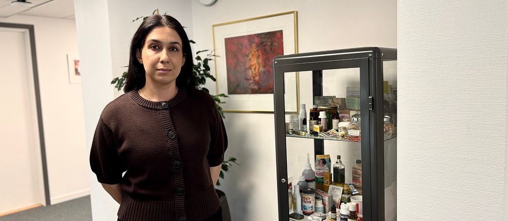 Apotekaren Shahabeh Shokrolahi står bredvid ett vitrinskåp med olika föremål.