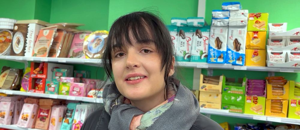 Person i en butik, omgiven av diverse matvaror på hyllor.