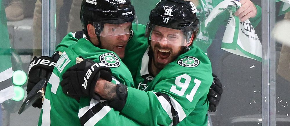 Två ishockeyspelare i gröna Dallas Stars-tröjor firar med en kram på isen.