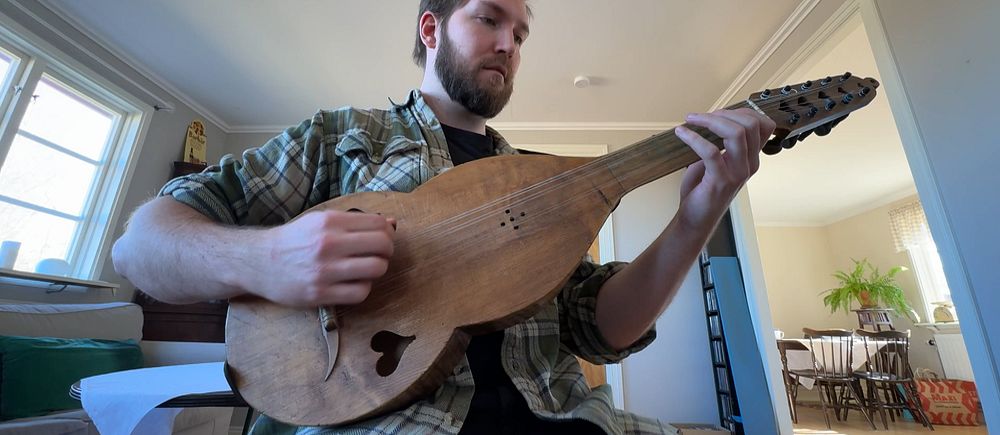 En person spelar en gammaldags luta i ett vardagsrum.