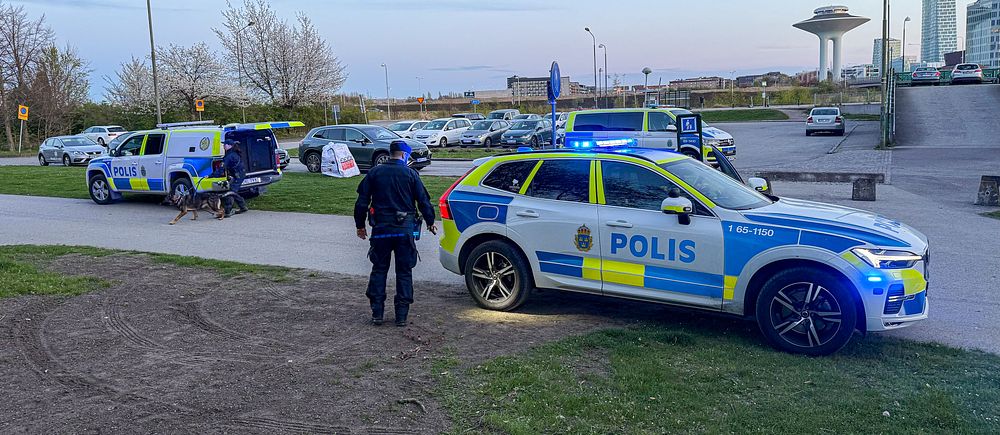 Flera polisbilar med blåljus och polis på plats vid parkering i ett bostadsområde.