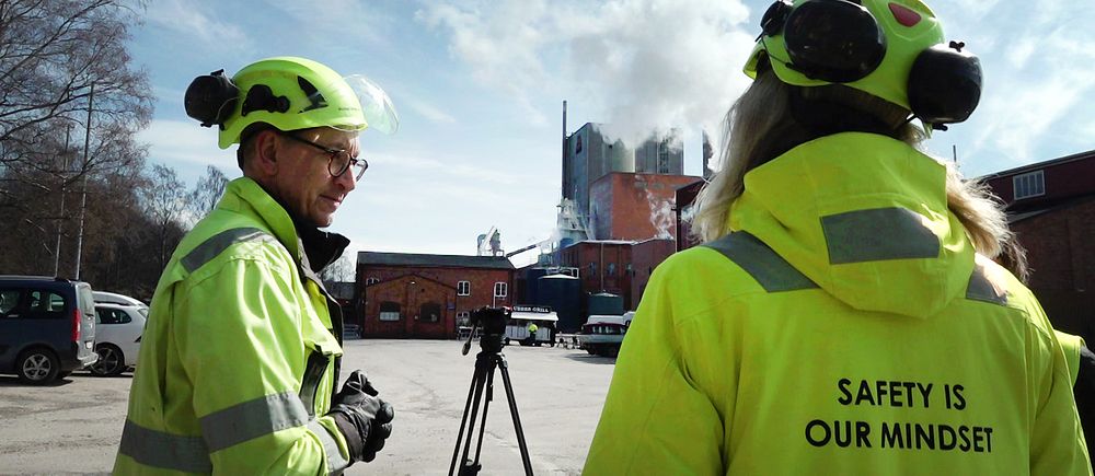 Två personer i ljusgrön varselklädsel och hjälmar vid Aspa bruk utanför Askersund, pratar om utsläpp från fabriken.