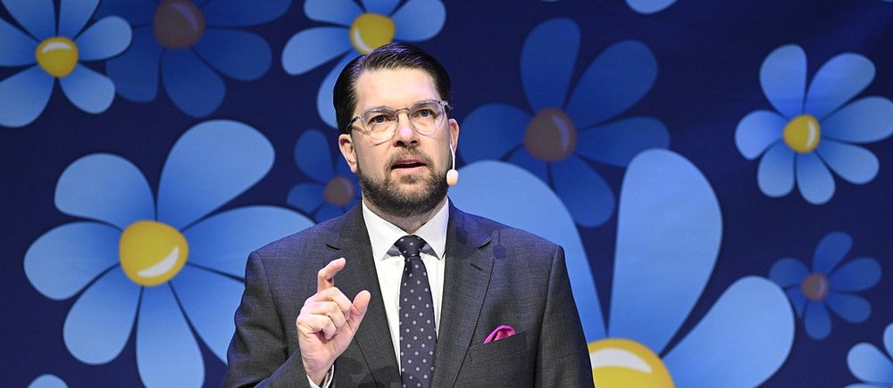Åkesson framför en fondvägg täckt av blommor.