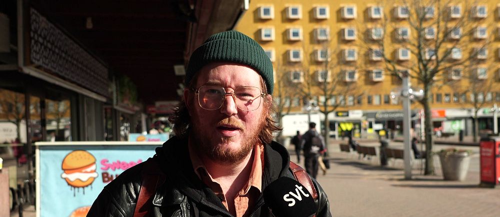 SVT intervjuar person på gata, orange byggnad i bakgrunden.