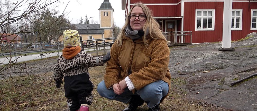 En förälder sitter på huk framför Himmeta skola på landsbygden utanför Köping. Bredvid står ett barn i förskoleålder.