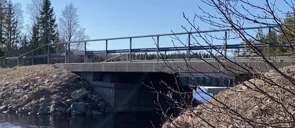 Bro över en stilla flod omgiven av träd och klarblå himmel.