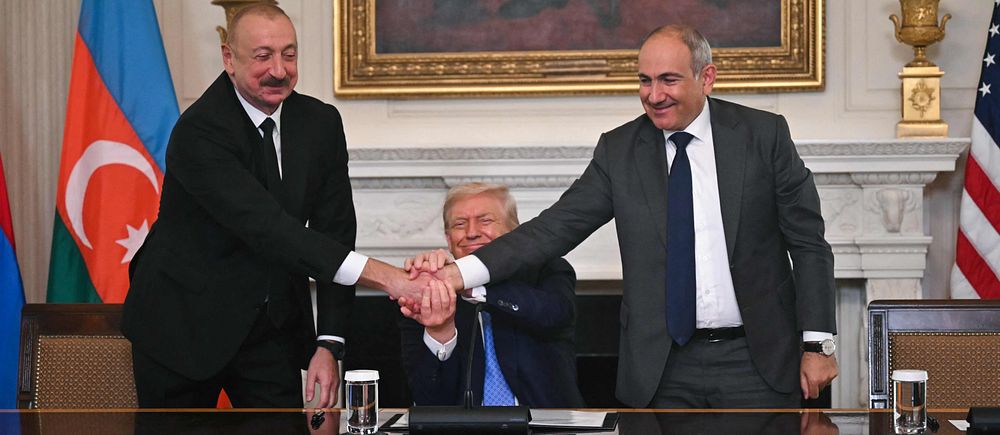 Donald Trump sitter mellan två personer som skakar hand vid ett mötesbord.