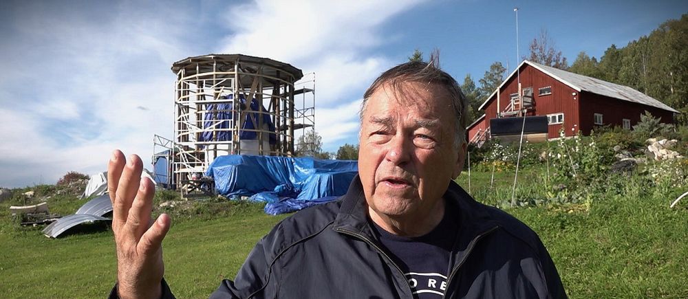 Man  i blå jacka står och gestikulerar framför en siloliknande byggnad i Salsån..