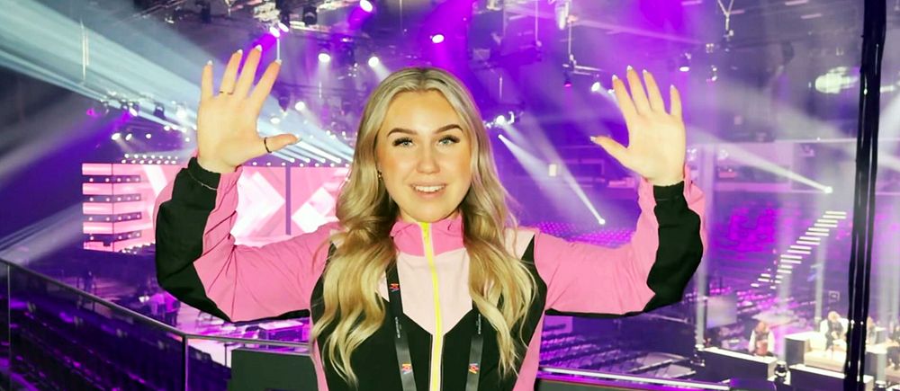 Lia Larsson står i Melodifestival-arenan med rosa kläder och händerna upp i luften