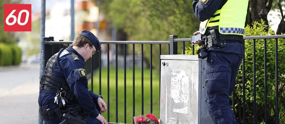 Två poliser vid ett blomhav på trottoaren, minnesplats efter händelse utomhus.