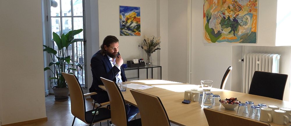 En man läser ett papper i ett soligt kontorsrum med konferensbord och konst på väggarna.