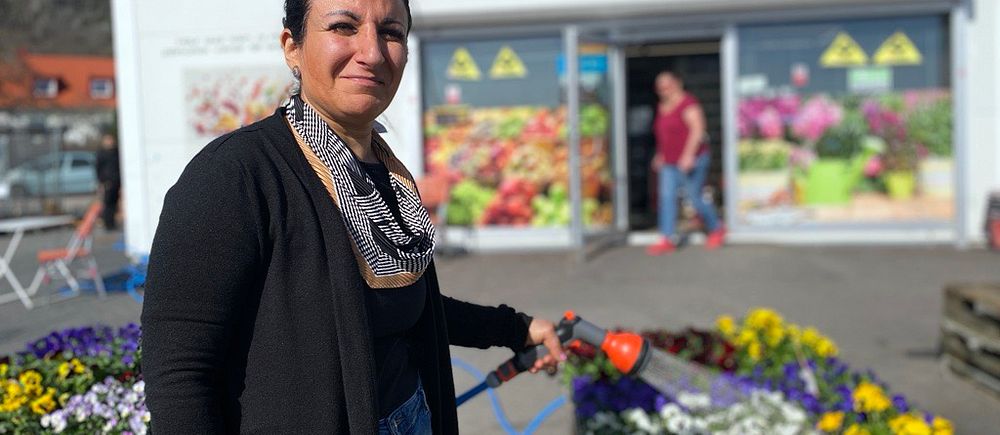 Kvinna vattnar blommor framför en butik