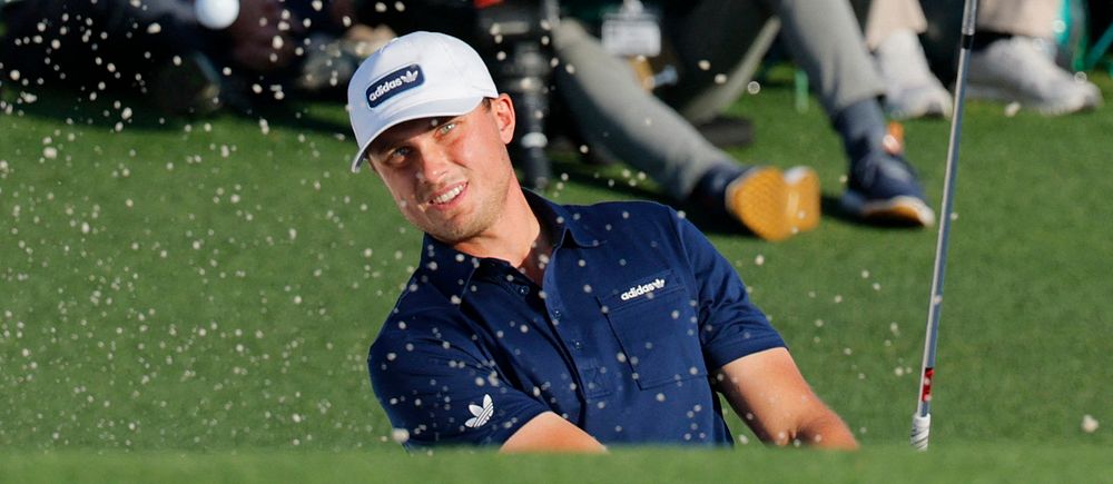 Golfspelare slår ett slag ur en sandbunker, sandpartiklar sprids i luften.