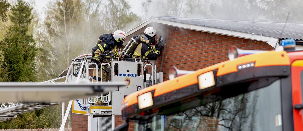 två brandmän arbetar med att släcka en brand på taket tillhörande en villa.