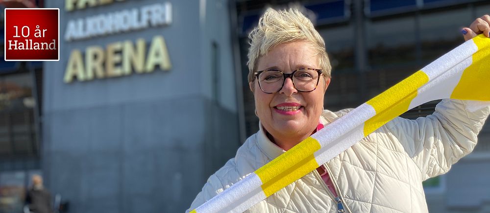 Mari-Louise Wernersson (C) håller en gul och vit sjal framför arenan ”Falcon Alkoholfri Arena”