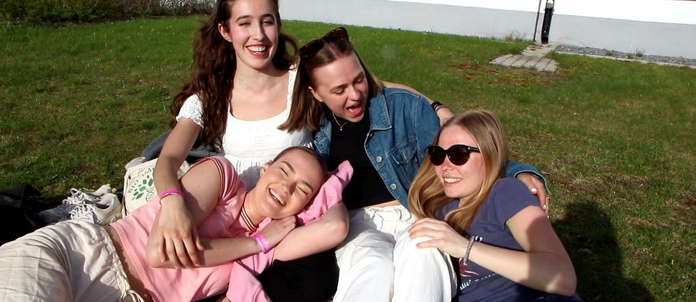 Fyra tjejer sitter på en filt på gräset och skrattar.
