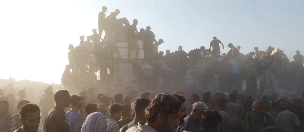 Stor folkmassa som väntar på nödhjälp samlad utomhus i Gaza i dammig miljö under starkt solljus.