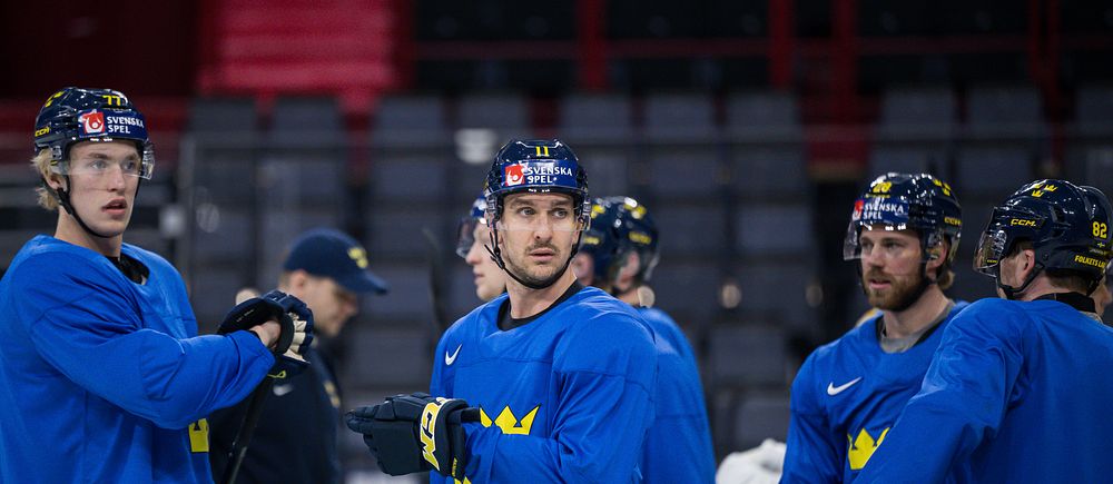 Ishockeyspelare i blå tröjor samtalar under ett träningspass i ishall.