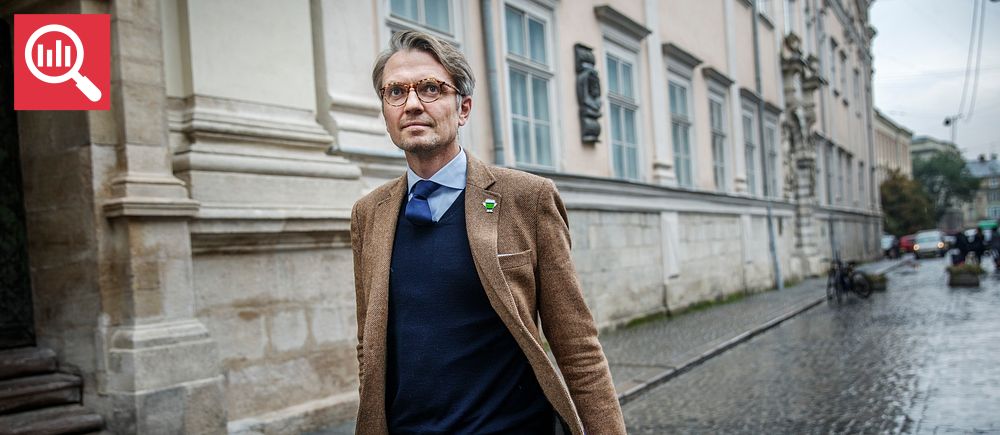 En man i brun kavaj går på en kullerstensgata utanför en äldre byggnad.