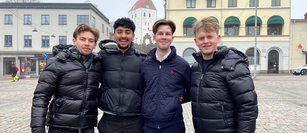 Fyra unga män poserar i vinterkläder på torget i Ronneby framför gamla byggnader.