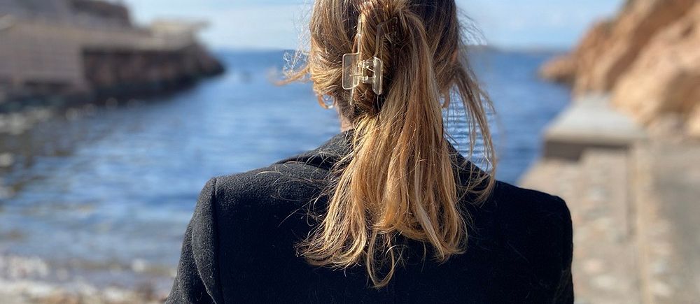 Kvinna står bortvänd från kameran mot havet