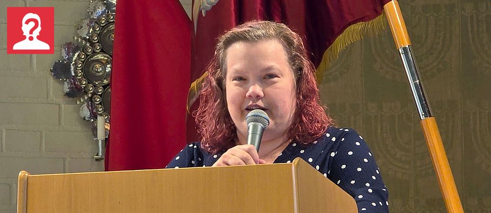 Sara Mårtensson håller tal vid ett podium med Socialdemokraternas logotyp och röda fanor i bakgrunden i samband med att hon presenteras som ny kommunalråd i Dorotea.
