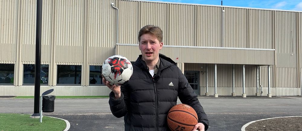 Person håller fotboll och basketboll framför sporthall.