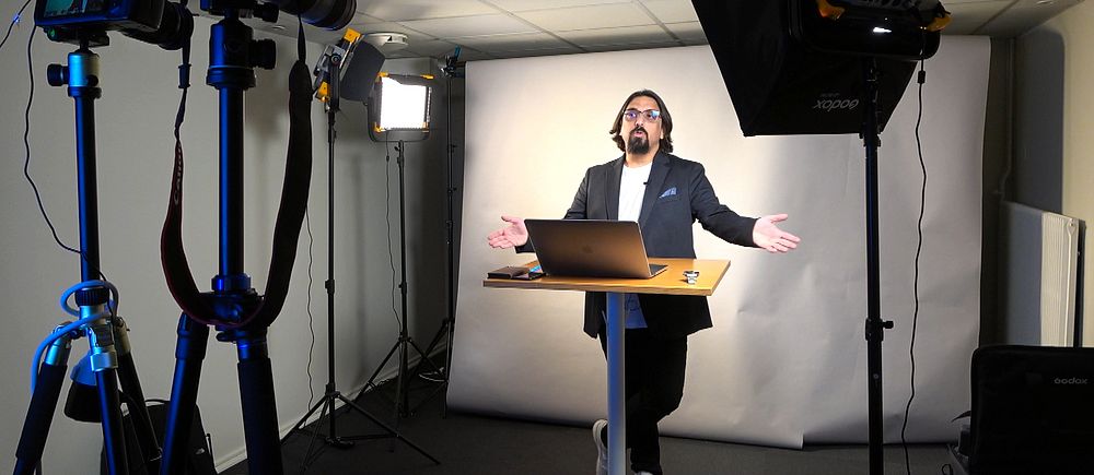 En person håller digital föreläsning framför kamera och strålkastare i studio.