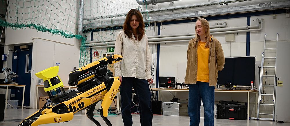 Två personer tittar på en gul fyrbent robot i ett laboratorium.