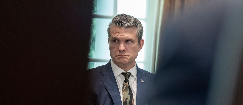 Man i kostym sitter vid ett bord i ett formellt mötesrum.