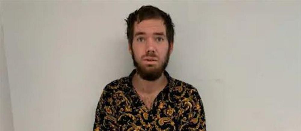 Person med mörkt, mönstrat skjorta står mot en vit vägg.