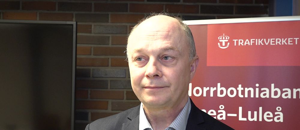 En man i kavaj framför en Trafikverketskylt.