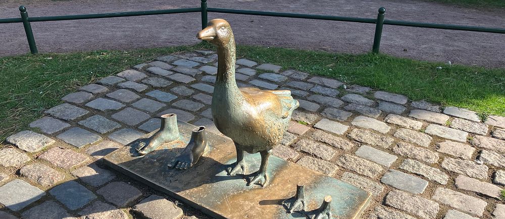 Staty av en gås med fötter kvar från avsågade fötter på stenbelagd mark i ett parkområde.