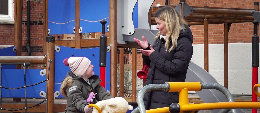 Mamma pratar teckenspråk med sitt barn på en lekplats.