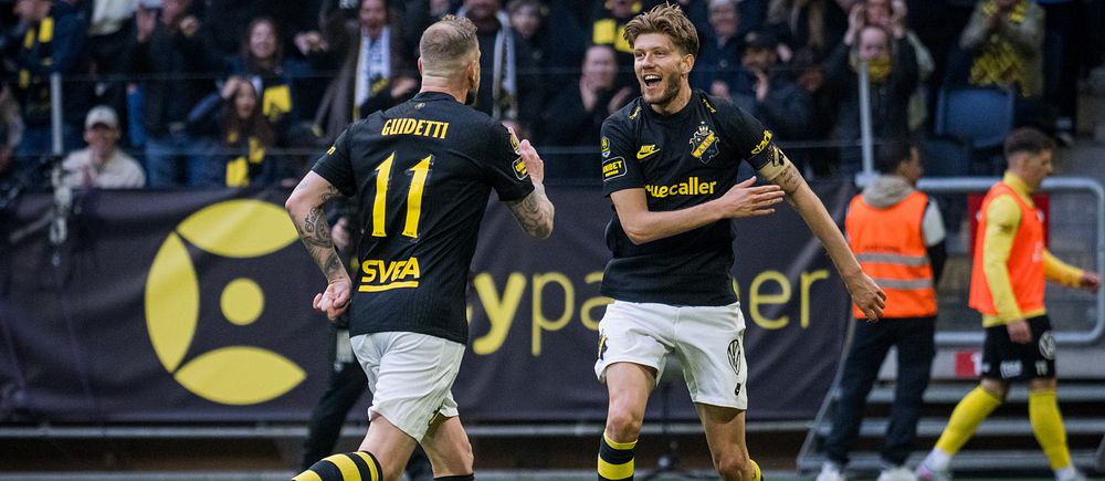 Två AIK-spelare firar mål inför jublande supportrar på fotbollsläktaren.