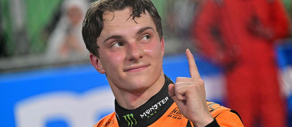 Racingförare i orange overall gör en segergest, pekar uppåt med fingret.