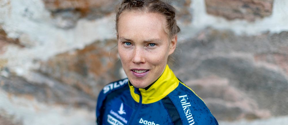 Person i blå-gul sporttröja, står framför en stenvägg.
