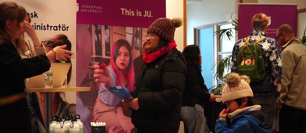 Personer diskuterar vid en monter på Campus Ronneby. Ett barn står bredvid en vinterklädd vuxen.