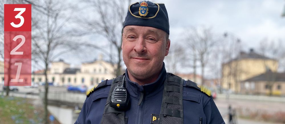 Polis med uniform och utrustning i stadsmiljö. Bakgrund med park och byggnader.