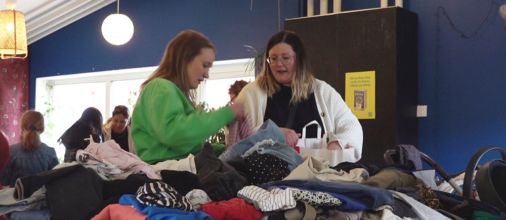 två kvinnor står och kollar bland kläder på en klädbytardag