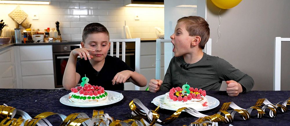 Tvillingpojkar sitter vid bord med varsin tårta framför sig