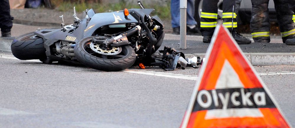 Omkullvält motorcykel, olycksvarningstriangel i förgrunden, brandmän i bakgrunden.