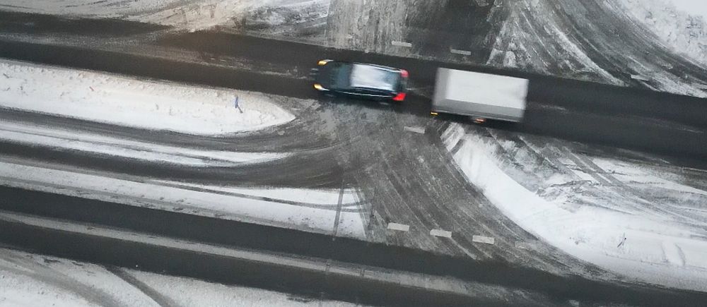 En bil med ett släp på en snöig väg. Bilden är tagen från ovan med en drönare.