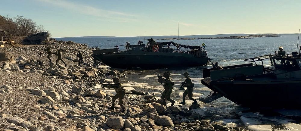 Soldater stiger i land från militärbåtar vid stenig kust.