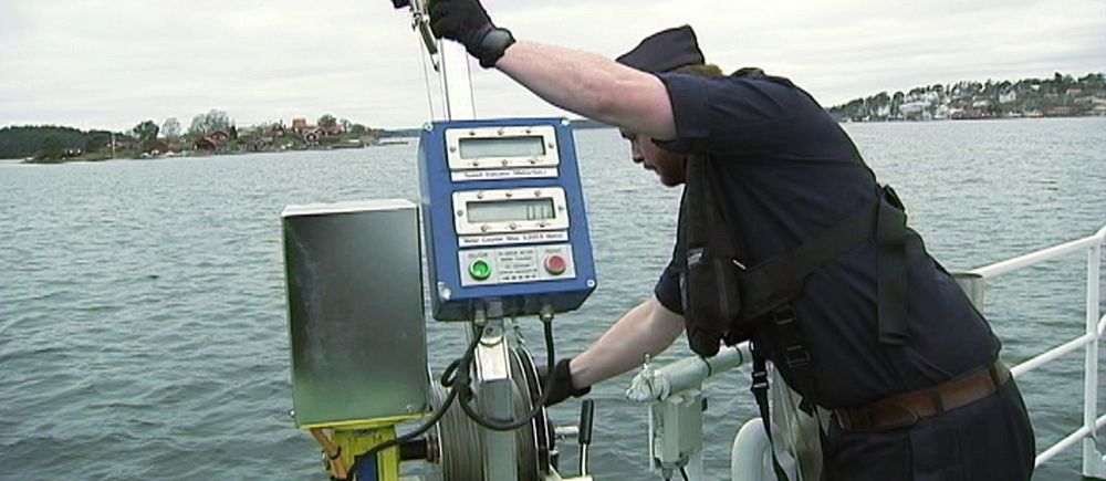 Man ombord på båt står vid relingen och håller i sjömätningsinstrument över vattenytan.