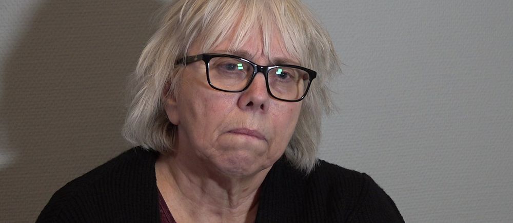 Kvinna med vitt hår som sitter mot en grå vägg